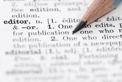 Close-up shot of the dictionary definition for "editor," with a pencil resting across part of the text.
