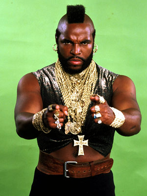 Mr T gazes and points with both hands directly at the camera. His sleeveless arms betray rippling biceps. This black, muscled icon stands silhouetted against a bright green back ground.