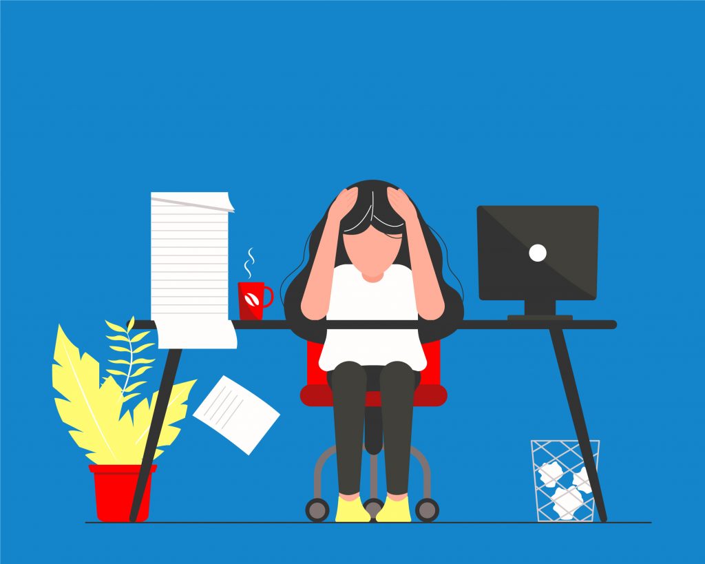 Person sitting at a desk with their head in their hands, with a computer, notepad and mug on the desk.
