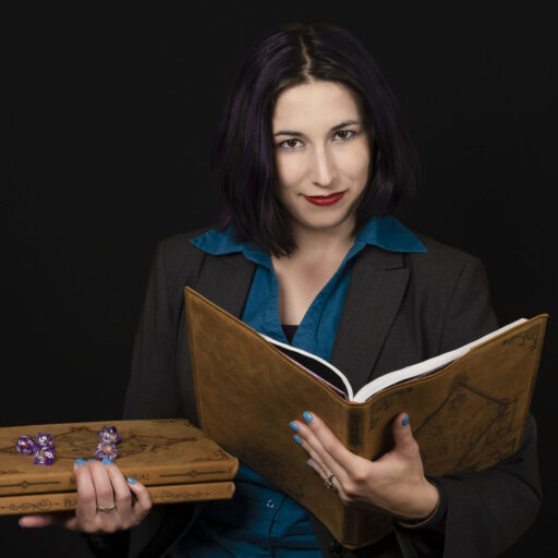 Heather Romanowski holds a leather-bound book open in one hand while holding a stack of similar books in her other hand. Atop the stack are multi-sided purple dice.